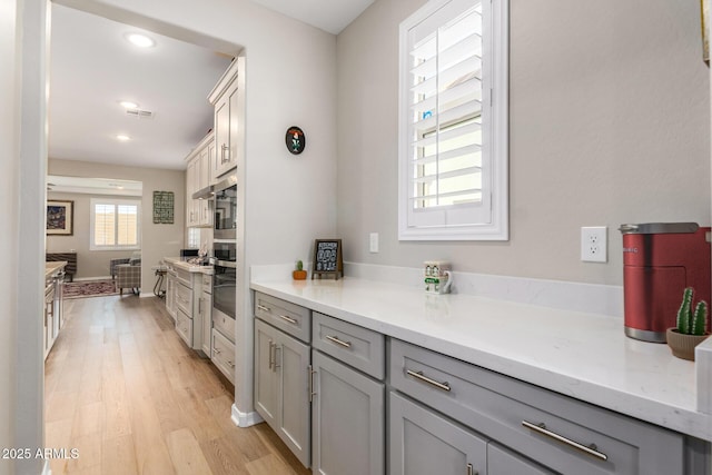 kitchen featuring light stone countertops, gray cabinetry, oven, and light hardwood / wood-style flooring