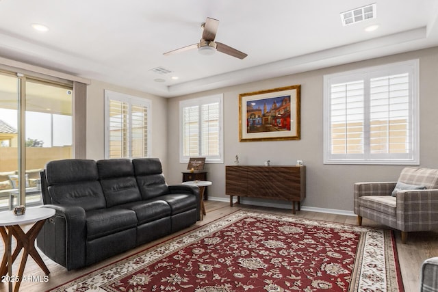 living room featuring ceiling fan, wood-type flooring, plenty of natural light, and a raised ceiling