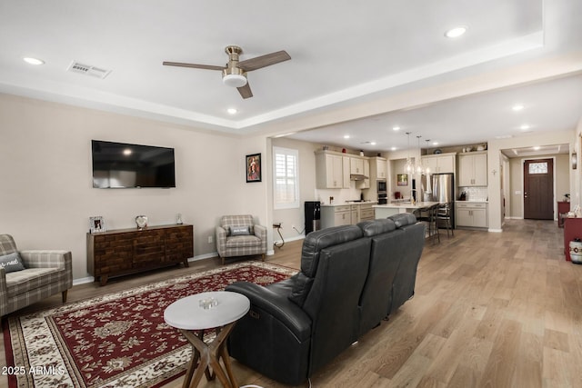 living room with ceiling fan, a tray ceiling, and light hardwood / wood-style floors