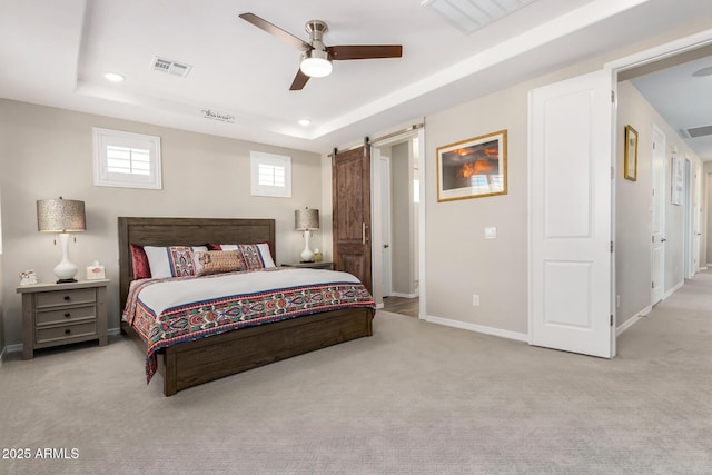 bedroom with ceiling fan, a barn door, light colored carpet, and a tray ceiling