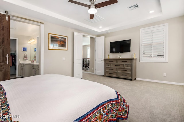 carpeted bedroom with ceiling fan, a raised ceiling, ensuite bath, and a barn door