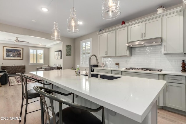 kitchen with tasteful backsplash, sink, stainless steel gas cooktop, a kitchen island with sink, and gray cabinetry