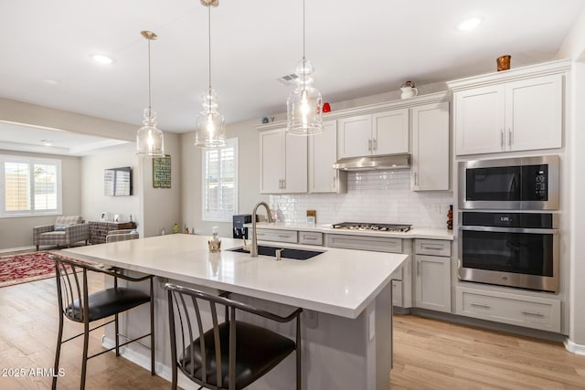 kitchen featuring a kitchen bar, a center island with sink, appliances with stainless steel finishes, hanging light fixtures, and sink