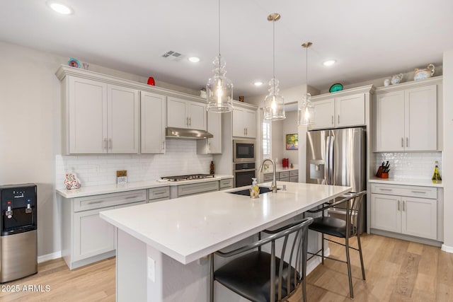 kitchen featuring decorative light fixtures, a center island with sink, light wood-type flooring, a kitchen breakfast bar, and stainless steel appliances