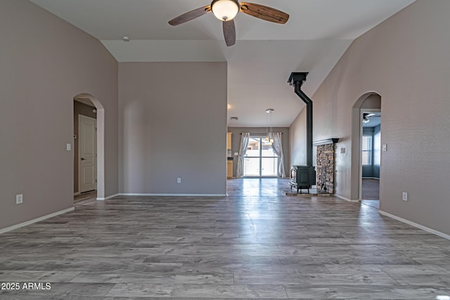 unfurnished living room featuring a ceiling fan, arched walkways, baseboards, and wood finished floors