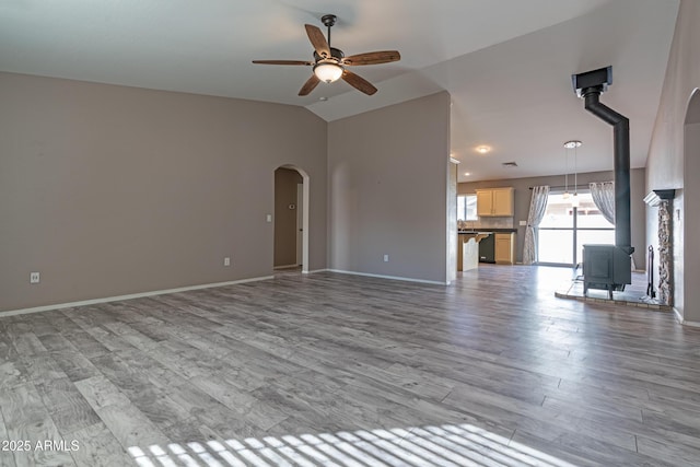 unfurnished living room with arched walkways, a ceiling fan, lofted ceiling, light wood-style flooring, and a wood stove