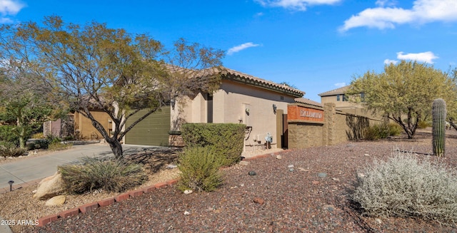 view of home's exterior featuring a garage, driveway, a tiled roof, and stucco siding