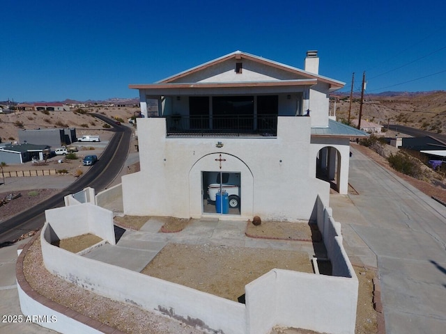 view of front facade featuring metal roof, a chimney, a balcony, and stucco siding