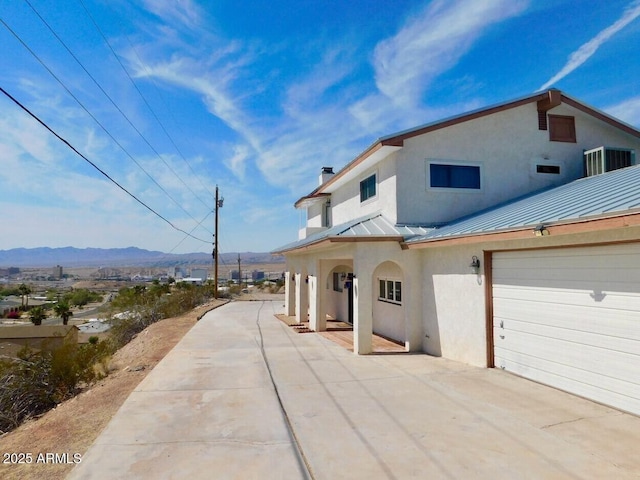 exterior space with metal roof, a mountain view, central air condition unit, stucco siding, and a standing seam roof