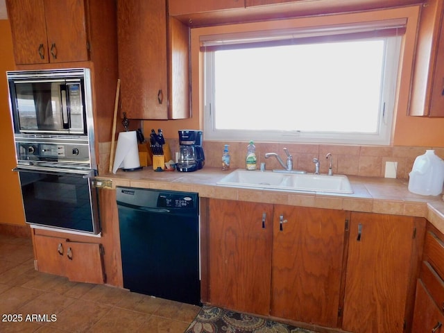 kitchen with plenty of natural light, a sink, tile countertops, and black appliances