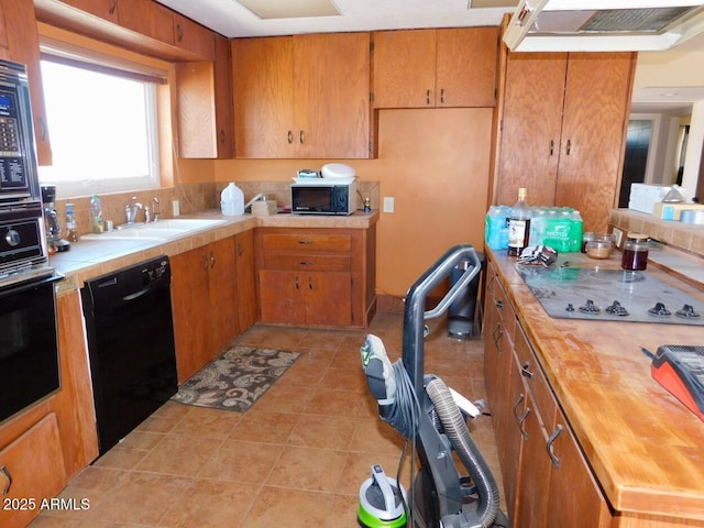 kitchen featuring brown cabinets, a sink, black appliances, and light tile patterned floors