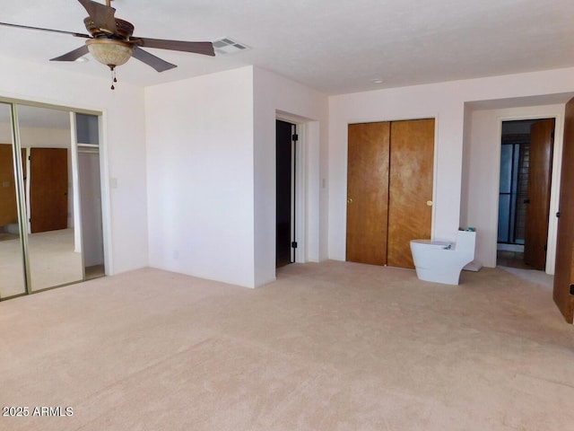 unfurnished bedroom featuring ceiling fan, two closets, visible vents, and light colored carpet