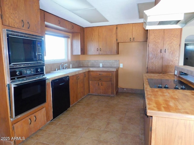 kitchen with butcher block countertops, a sink, ventilation hood, brown cabinets, and black appliances