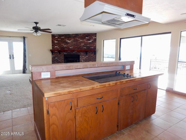 kitchen featuring a brick fireplace, open floor plan, light tile patterned flooring, under cabinet range hood, and black electric cooktop