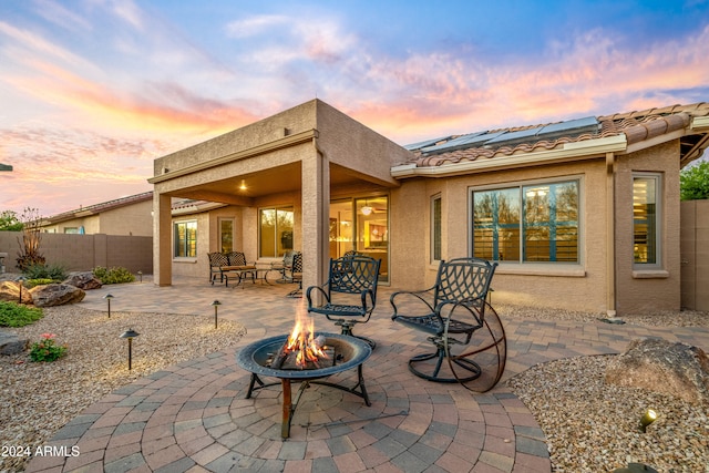 back house at dusk with solar panels, an outdoor fire pit, and a patio