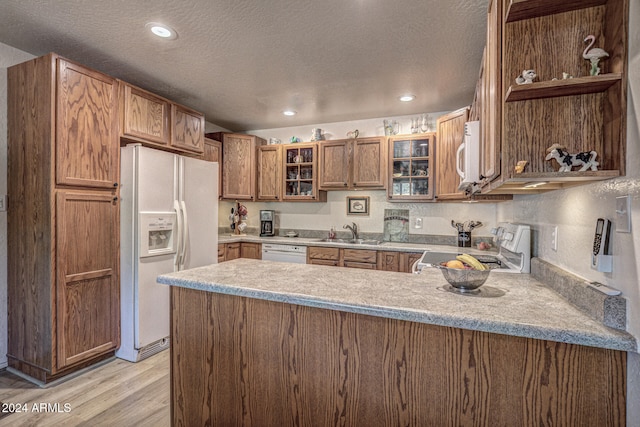 kitchen featuring sink, light hardwood / wood-style flooring, a textured ceiling, kitchen peninsula, and white appliances