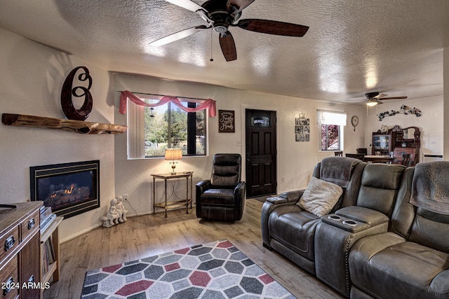 living room featuring ceiling fan, light hardwood / wood-style flooring, and a textured ceiling