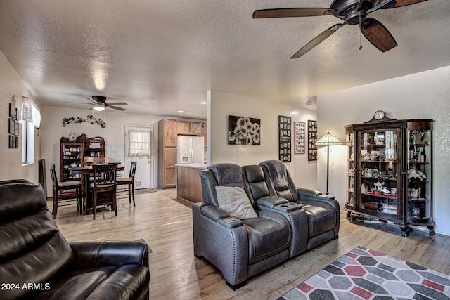 living room featuring ceiling fan, a textured ceiling, and light wood-type flooring