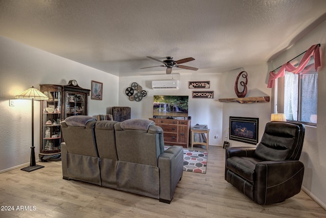 living room with ceiling fan, a wall mounted air conditioner, a textured ceiling, and light wood-type flooring