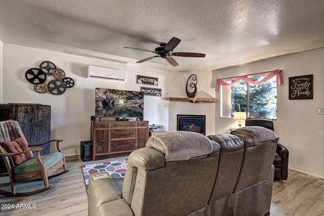 living room with ceiling fan, a textured ceiling, light hardwood / wood-style flooring, and an AC wall unit