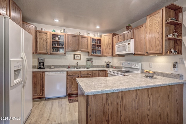 kitchen with sink, white appliances, light hardwood / wood-style floors, and kitchen peninsula