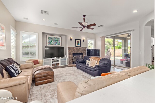 living room with a stone fireplace, ceiling fan, and a wealth of natural light