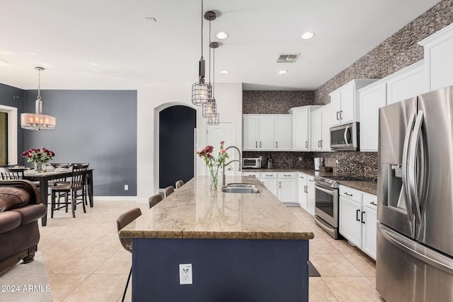 kitchen with white cabinetry, light stone countertops, an island with sink, decorative light fixtures, and appliances with stainless steel finishes