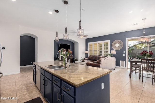 kitchen featuring a center island with sink, sink, hanging light fixtures, ceiling fan, and light stone counters