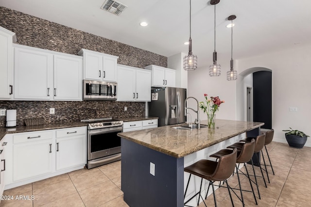 kitchen with appliances with stainless steel finishes, sink, dark stone countertops, hanging light fixtures, and an island with sink