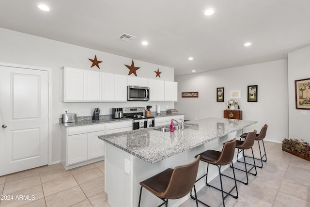 kitchen featuring a kitchen bar, stainless steel appliances, sink, white cabinetry, and an island with sink