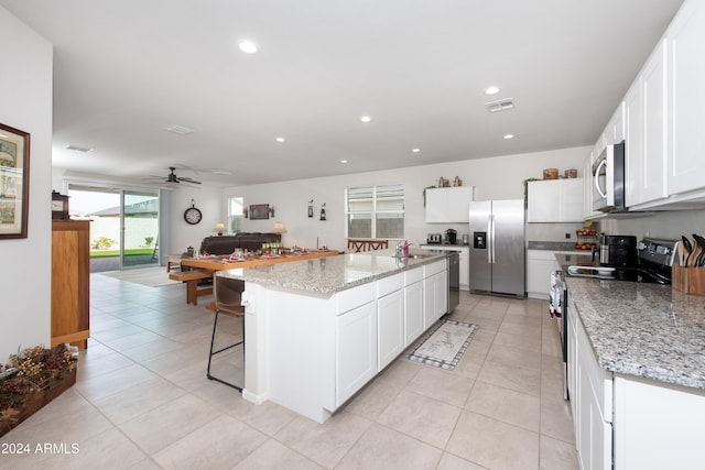 kitchen featuring light stone countertops, stainless steel appliances, ceiling fan, white cabinets, and a kitchen island