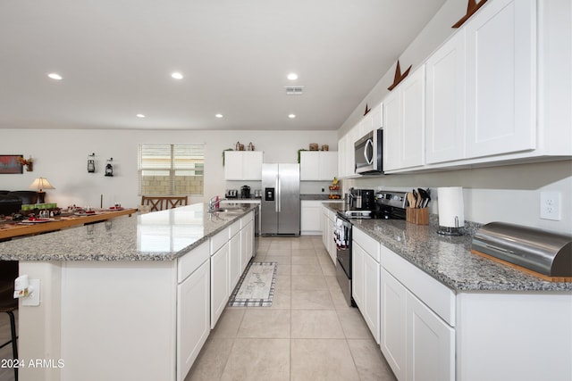 kitchen featuring stainless steel appliances, white cabinetry, a kitchen island with sink, and light stone counters