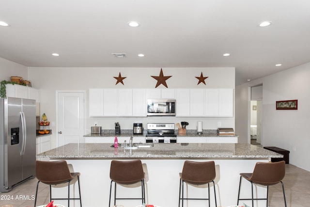 kitchen with white cabinets, stainless steel appliances, a kitchen island with sink, and a breakfast bar area