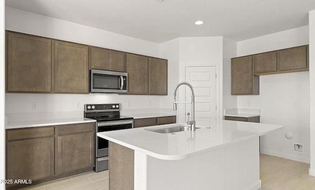 kitchen with stainless steel appliances, a sink, dark brown cabinets, light countertops, and an island with sink