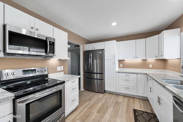 kitchen featuring appliances with stainless steel finishes, light wood-type flooring, white cabinets, and light stone counters