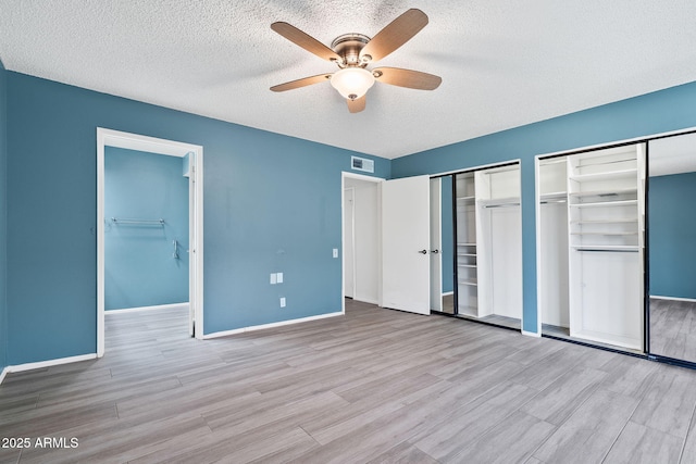 unfurnished bedroom featuring a textured ceiling, wood finished floors, visible vents, baseboards, and two closets