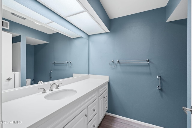 bathroom featuring baseboards, visible vents, toilet, wood finished floors, and vanity