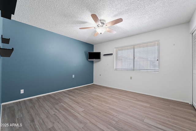 spare room featuring ceiling fan, a textured ceiling, baseboards, and wood finished floors