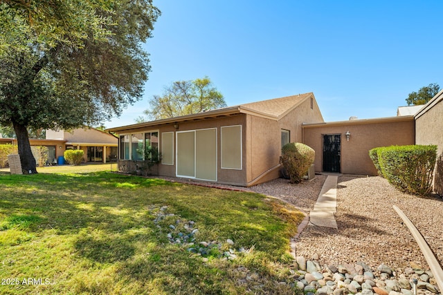 rear view of house featuring stucco siding and a yard