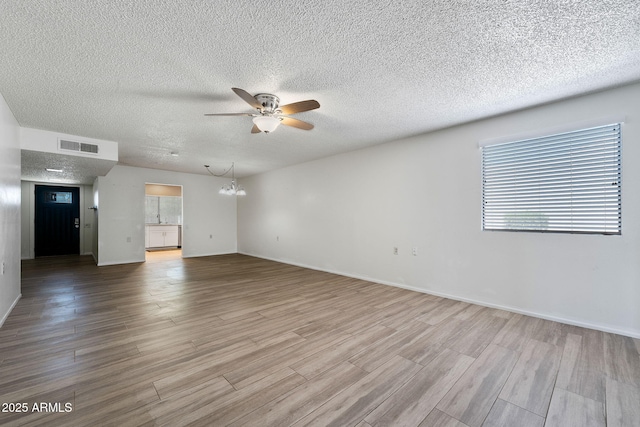 unfurnished living room with ceiling fan with notable chandelier, a textured ceiling, wood finished floors, and visible vents