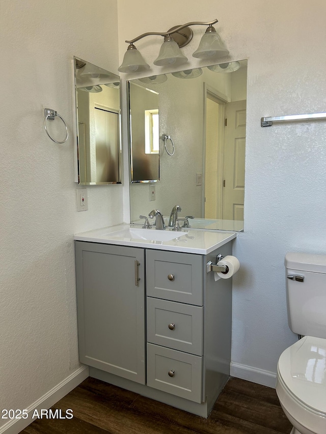 bathroom with toilet, baseboards, wood finished floors, and vanity