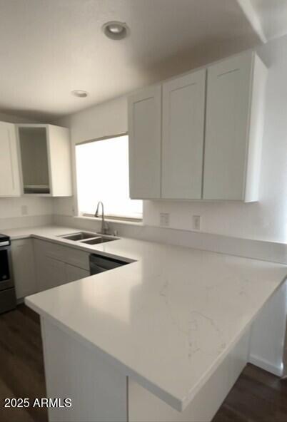 kitchen featuring a peninsula, dark wood finished floors, light countertops, a sink, and range
