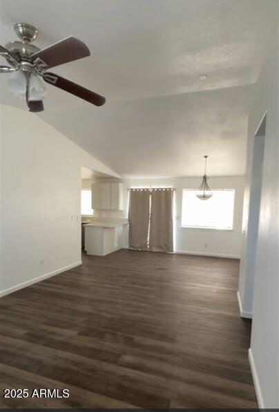 unfurnished living room with ceiling fan, vaulted ceiling, dark wood-style floors, and baseboards