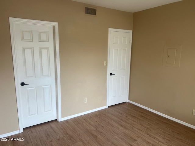 unfurnished bedroom with electric panel, wood finished floors, visible vents, and baseboards