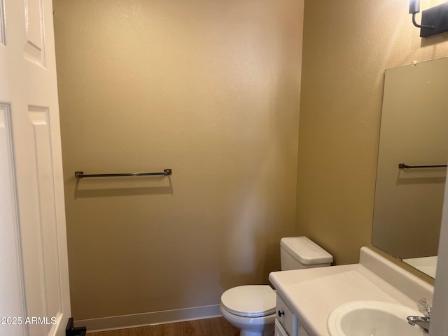 bathroom featuring toilet, vanity, baseboards, and wood finished floors