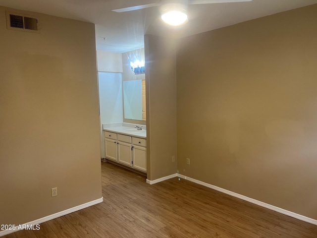 spare room featuring wood finished floors, a ceiling fan, visible vents, baseboards, and a sink