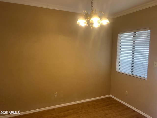 spare room featuring an inviting chandelier, crown molding, wood finished floors, and baseboards