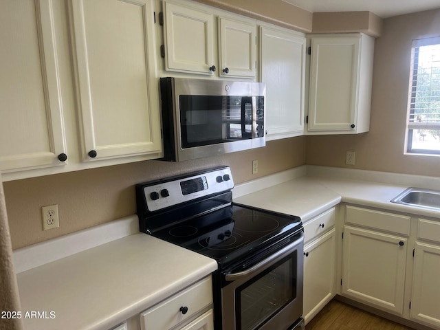 kitchen featuring a sink, wood finished floors, white cabinetry, appliances with stainless steel finishes, and light countertops