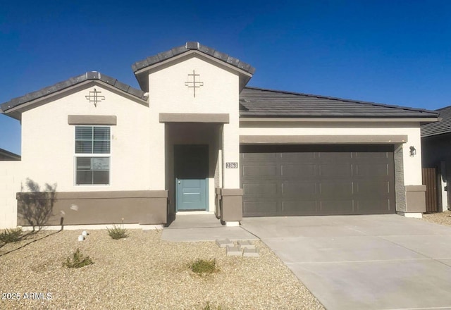 view of front of home featuring stucco siding, driveway, a tile roof, and a garage