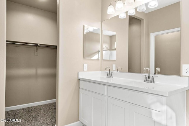full bath featuring baseboards, double vanity, a walk in closet, and a sink